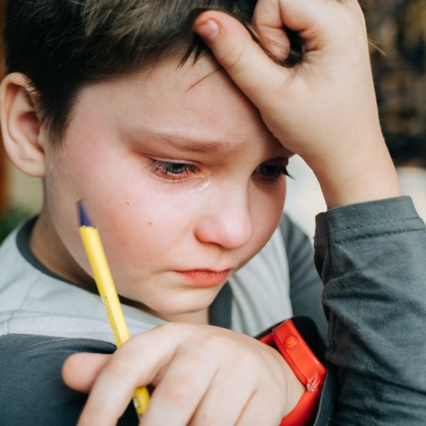 Crying unhappy child boy holding a pen while doing school homework.